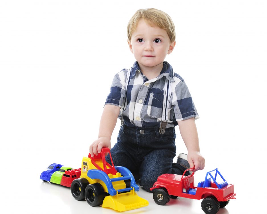 An adorable toddler looking up as he plays with her cars and trucks. On a white background.